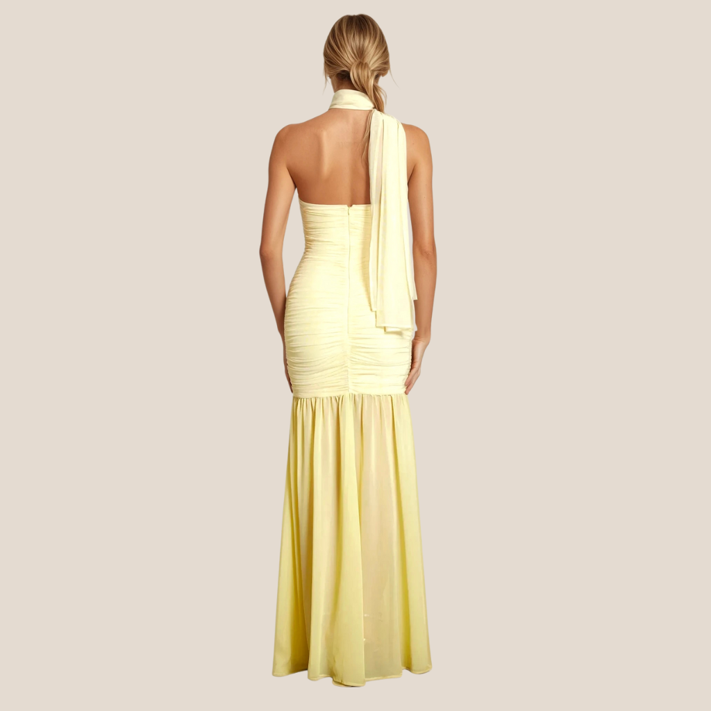 Model in pastel yellow ruched gown featuring halter neckline with draped mesh bust and flowy semi-sheer fishtail hem